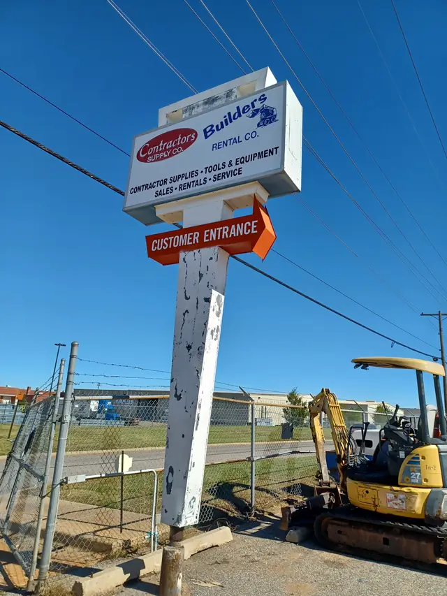 The Contractors Supply Co pylon sign on NE 30th Street reading contractor supplies, tools and equipment, sales, rentals, service, with a mini excavator on the lot behind