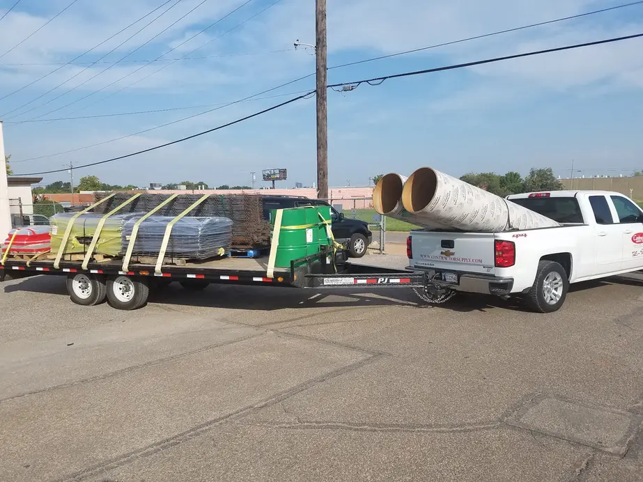 The Contractors Supply Co delivery truck towing a flatbed loaded with rebar, wire mesh pallets and concrete form tubes